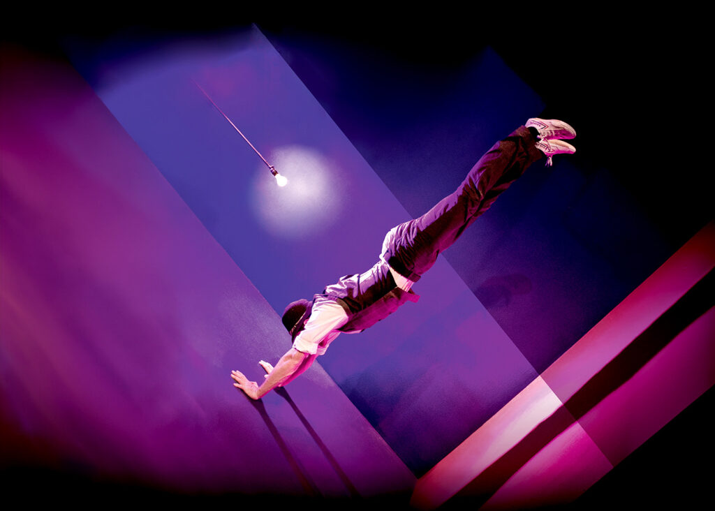 Auf dem Bild sieht man einen Mann, der auf einem schräg aussehenden Boden einen Handstand macht.