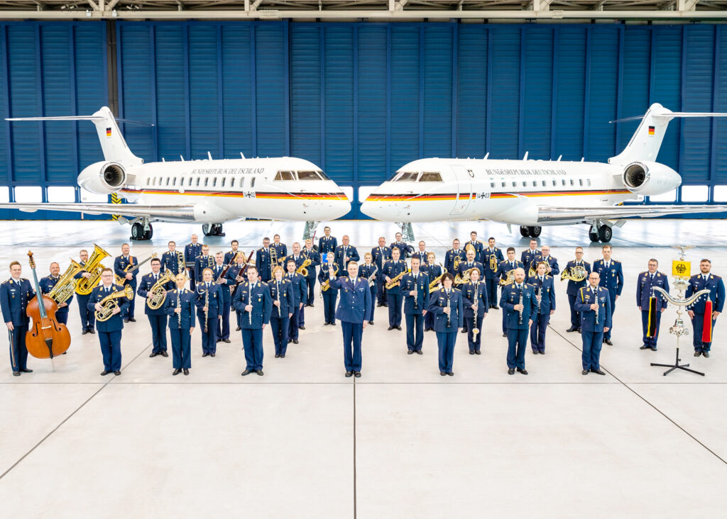 Auf dem Foto sieht man im Vordergrund das Luftwaffenmusikkorps Münster und im Hintergrund Auf dem Foto sieht man im Vordergrund das Luftwaffenmusikkorps Münster und im Hintergrund zwei Bundeswehrflugzeuge.