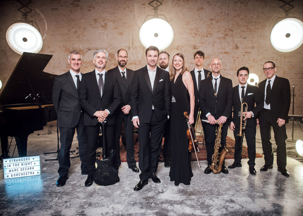 Auf dem BIld sieht man den deutschen Komponisten Marc Secara und sein mit auftretendes Orchestra.