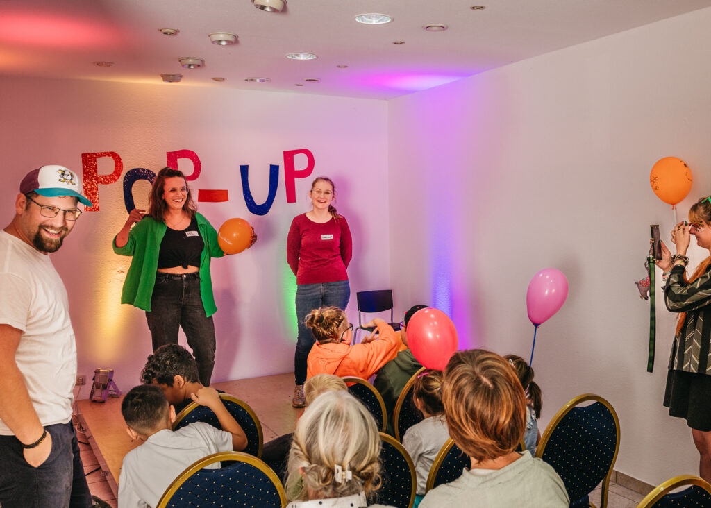 Das Bild zeigt die Kulturvermittlerin Miriam Engelmann in Aktion mit jungen Talenten auf der kleinen Bühne des Pop-Up Theaters.