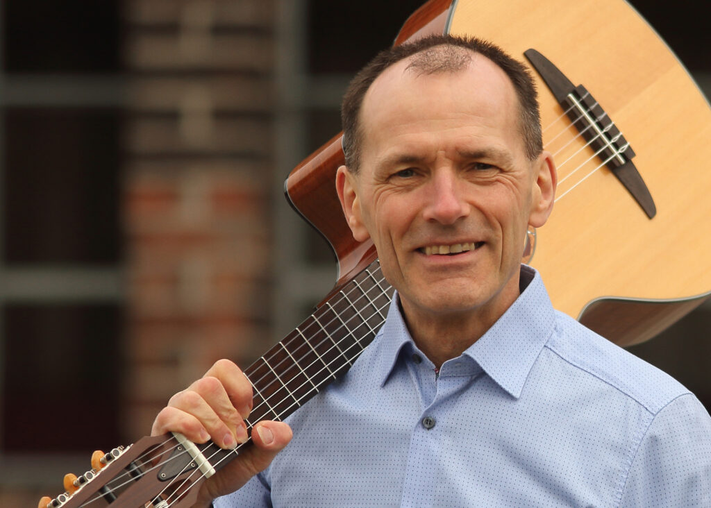 Stefan Nussbaum hat seine Gitarre auf der Schulter und lächelt in die Kamera.