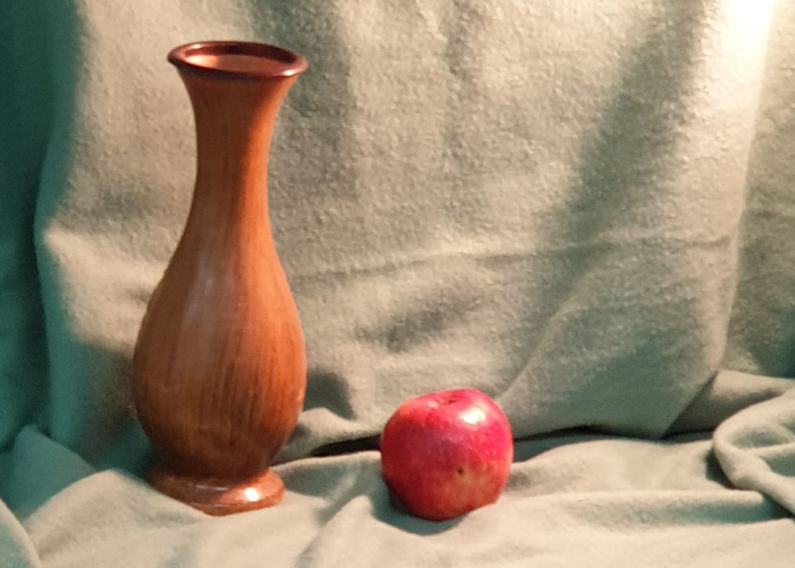 Eine Vase und ein Apfel stehen als Motive auf einer Decke, um sie zu malen.
