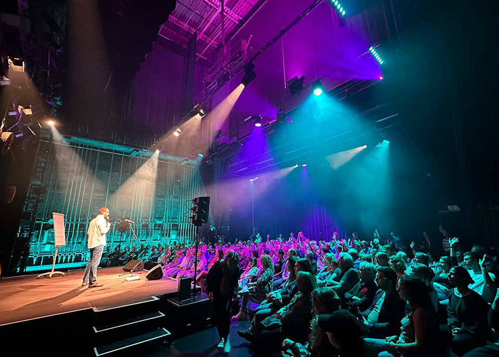 Bunt beleuchtete Hinterbühne im Industriecharme eines Theater, seitlich die Bühne mit einem Poetry-Slammer, davor volle Publikumsreihen.
