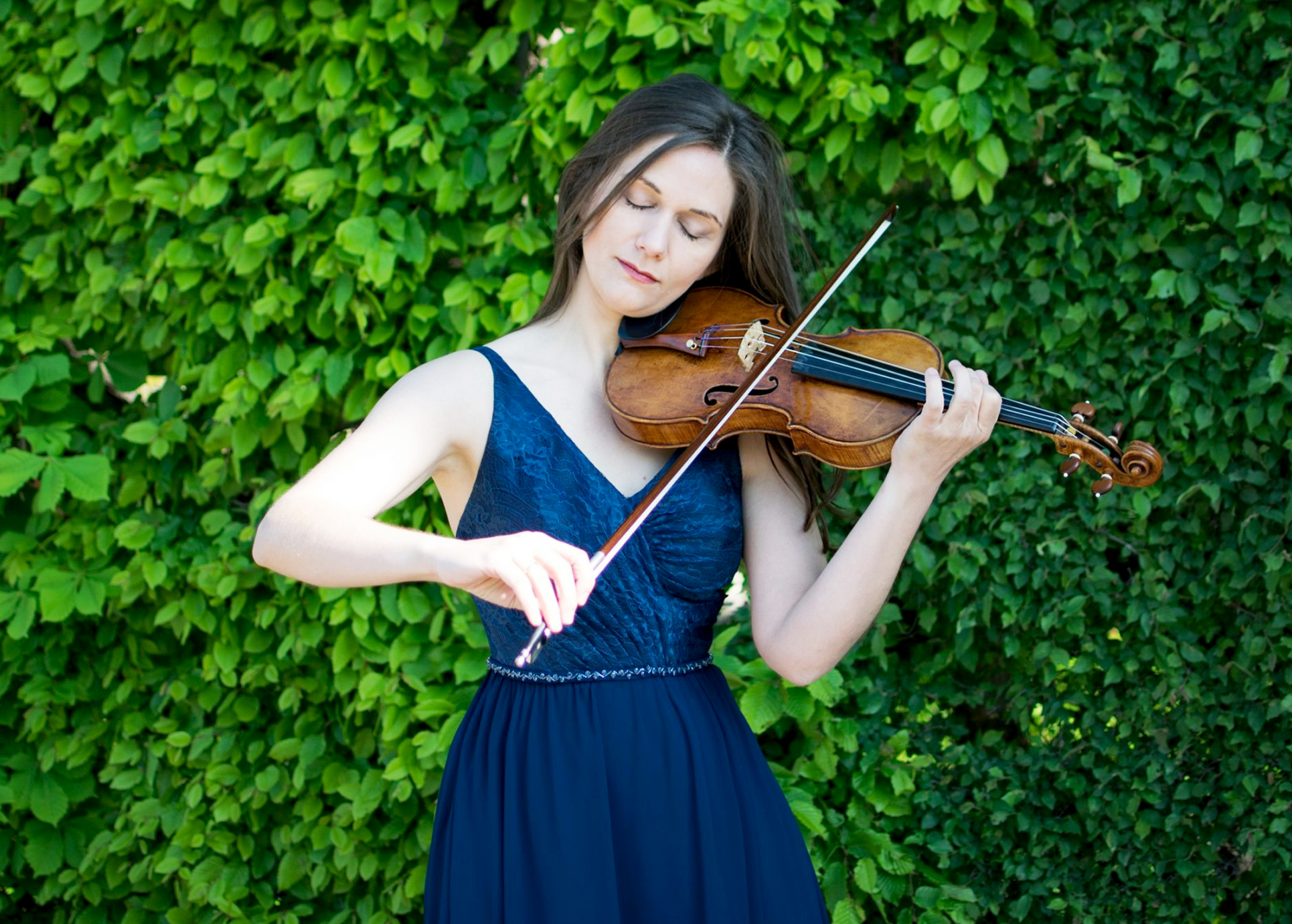 Violinistin Lena Neudauer spielt vor einer grünen Pflanzenwand hingebungsvoll auf ihrem Instrument.
