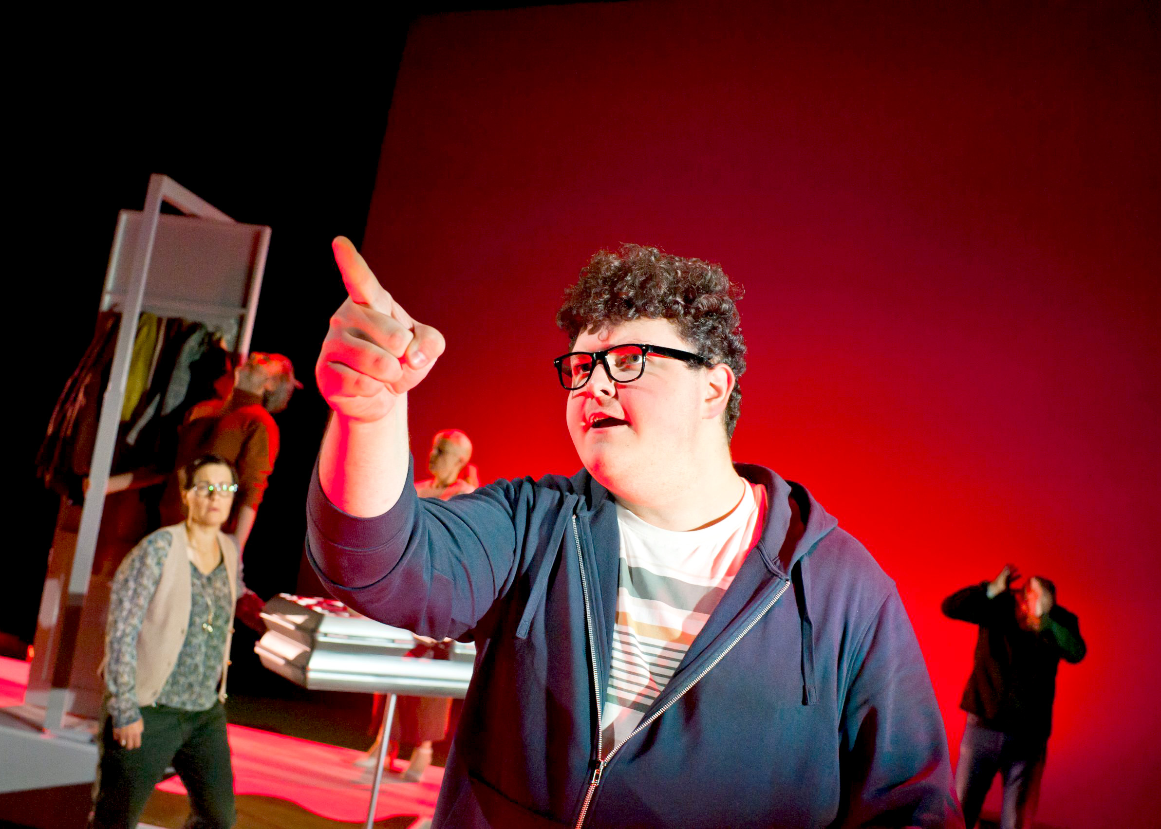 Schauspieler auf der Bühne, welcher mit erhobenem Finger auf die linke Seite zeigt.