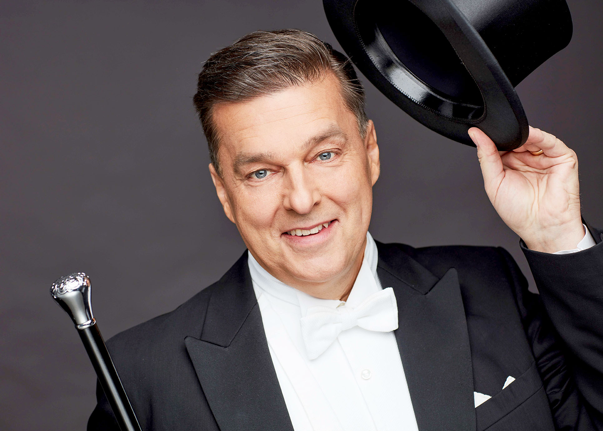 Das Foto zeigt Stefan Rex, der einen Zylinder und einen Dirigierstock in der Hand hält.