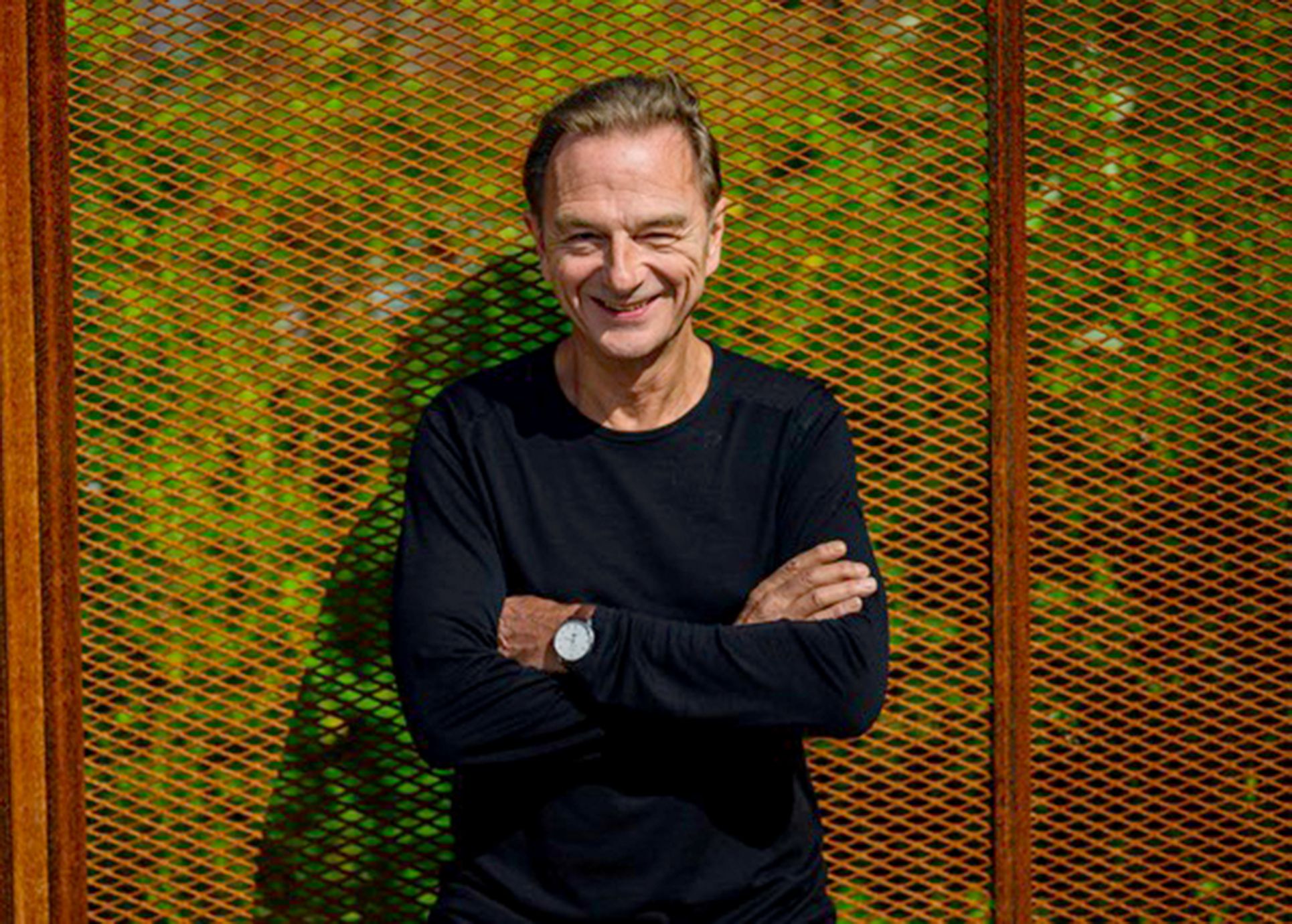 Fritz Eckenga steht mit verschränkten Armen vor einem Gitter und lächelt
