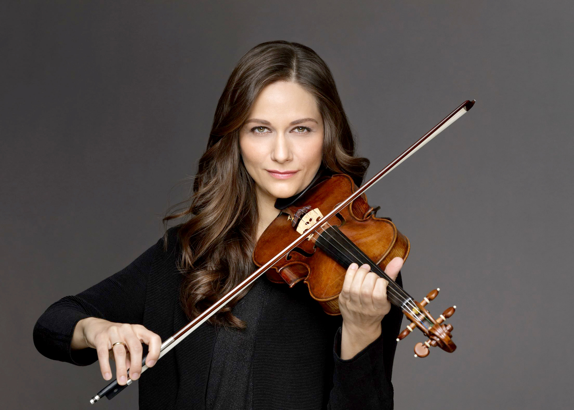 Violinistin Lena Neudauer hält ihr Instrument in der Hand. Der Bogen ist zum Spielen bereit und sie schaut direkt und auffordernd in die Kamera.