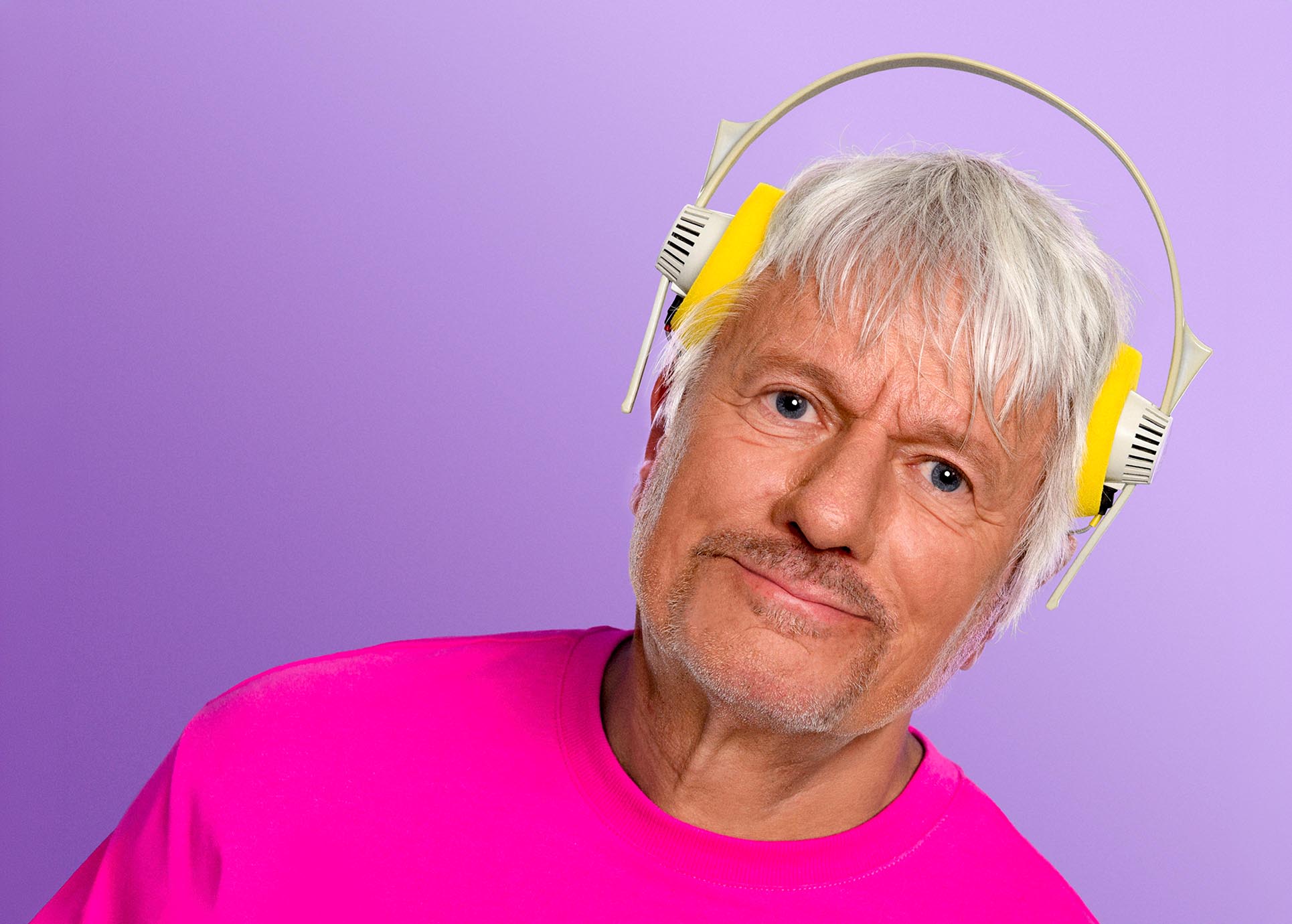 Jürgen Becker trägt Kopfhörer, die viel zu hoch über seinen Ohren auf dem Kopf sitzen