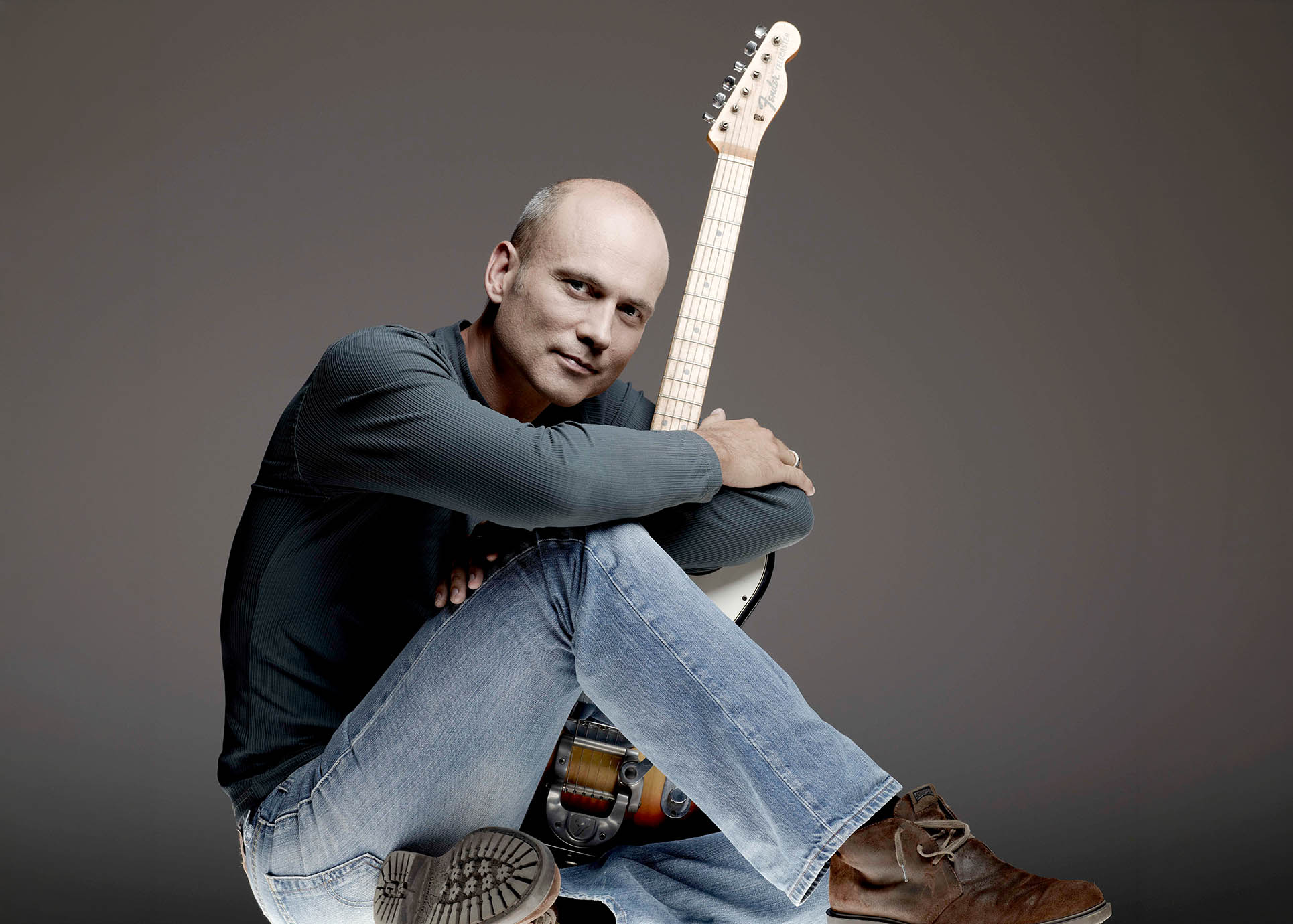 Oliver Steller sitzt auf dem Boden und umarmt eine Gitarre