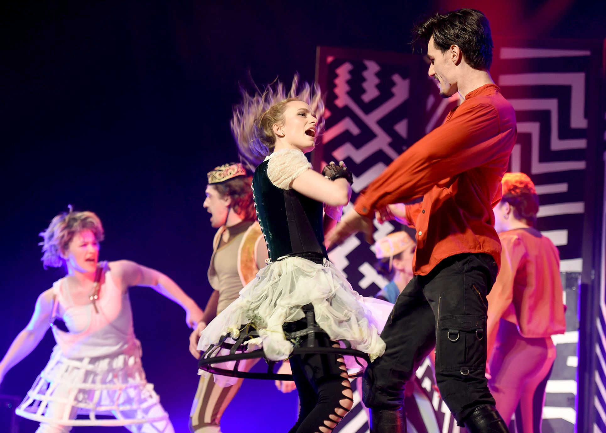 Theaterszene mit mehreren Darstellern, die tanzen.