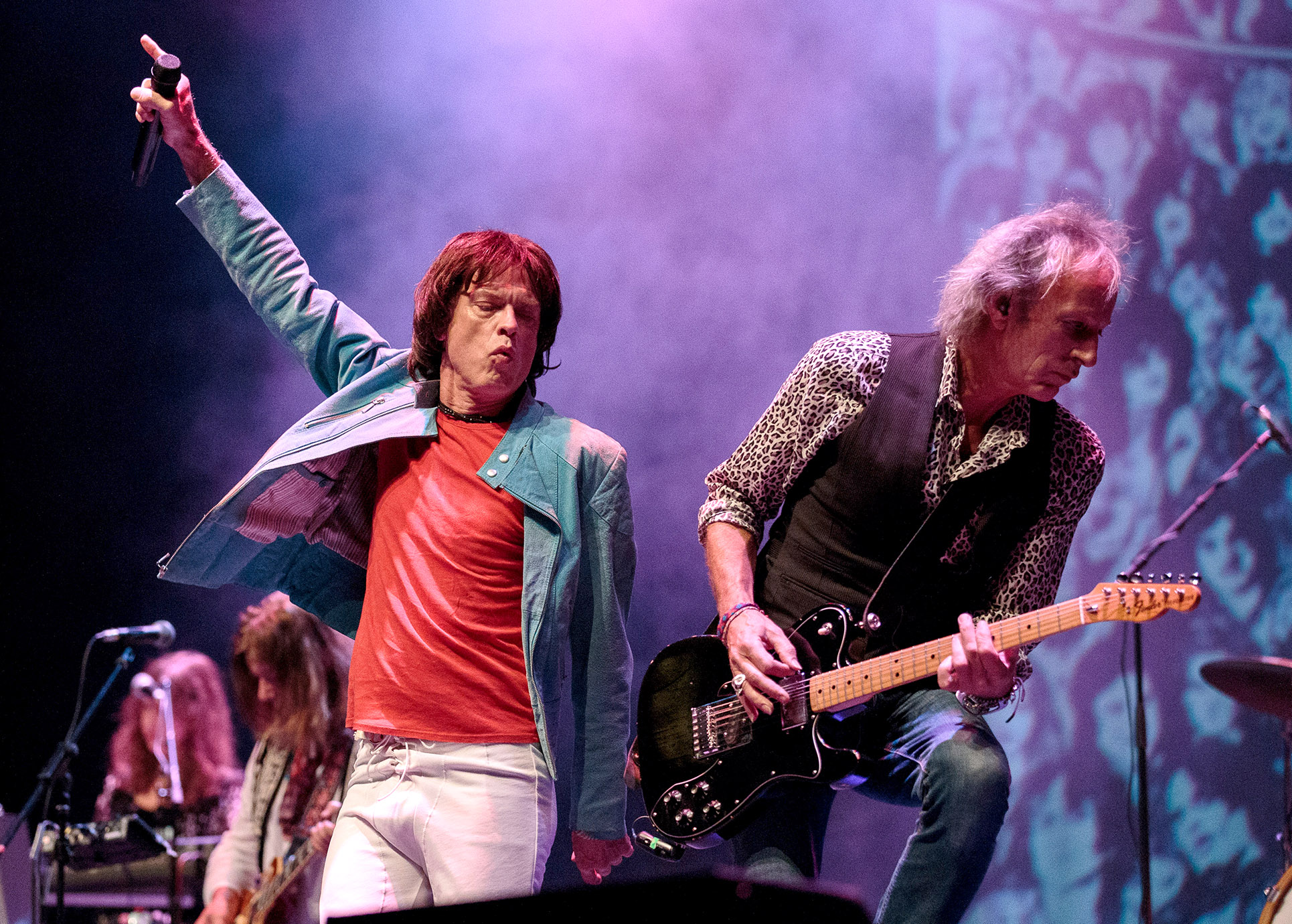 Auf dem Bild sieht man 2 Rocksänger auf der Bühne. Einer von beiden spielt auf der E-Gitarre der andere schaut ihm dabei zu.