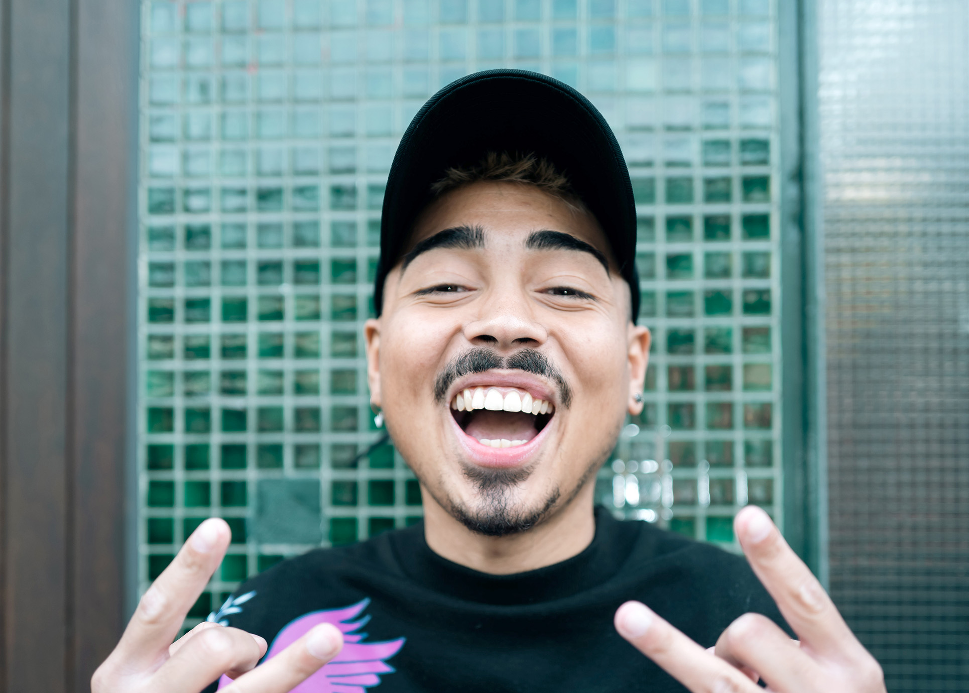 Comedian Tony Bauer lacht in die Kamera und zeigt den Rockergruß.