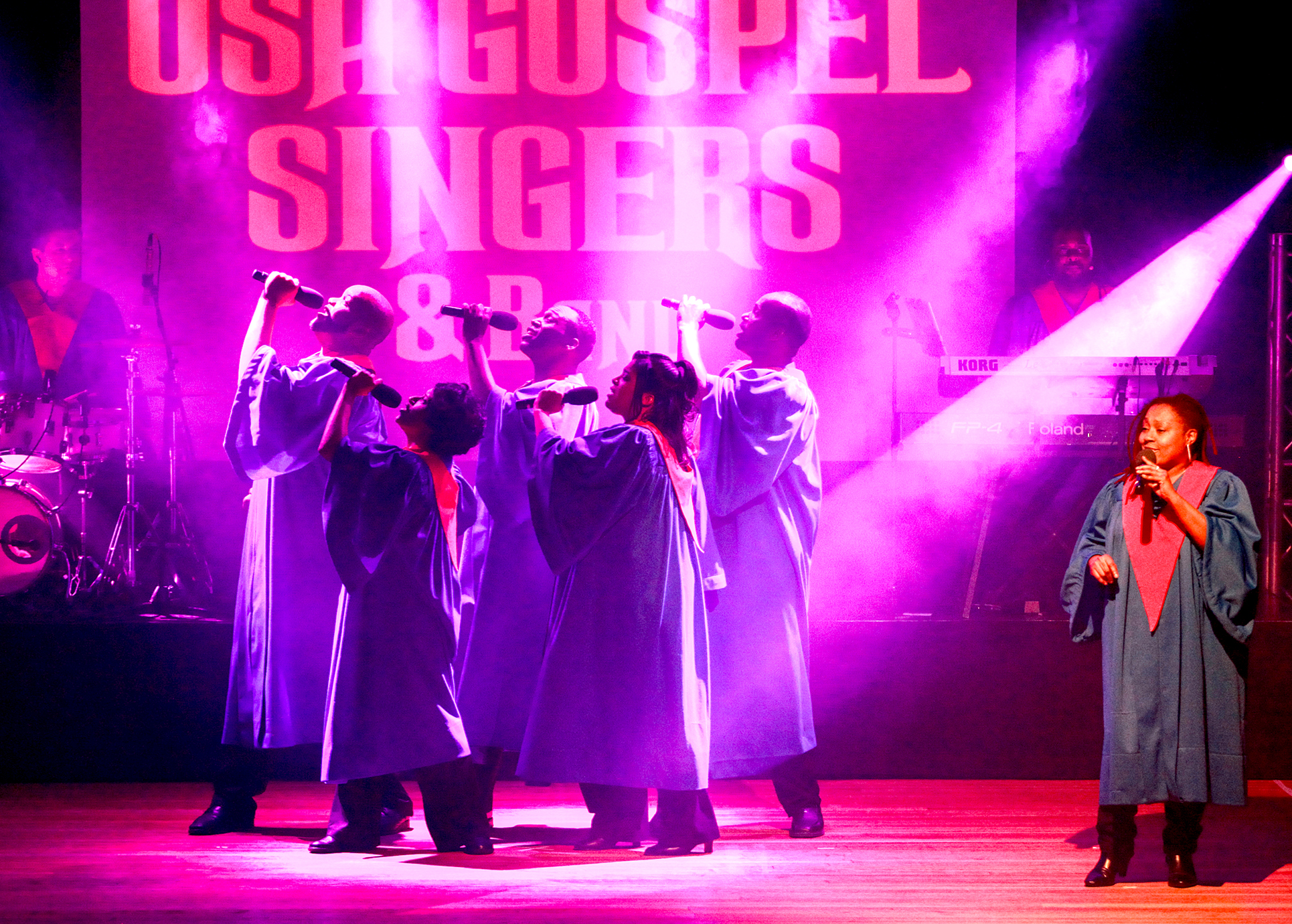 6 Gospelsänger und Sängerinnen auf der Bühne in pinkem Bühnenlicht