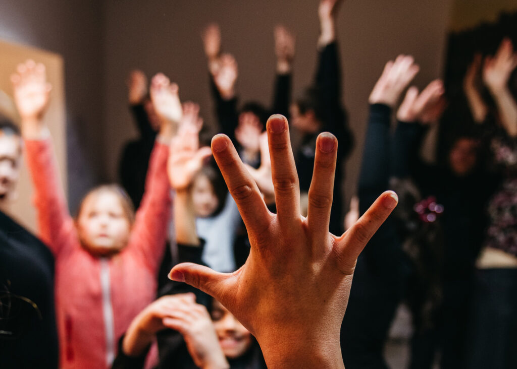 Mehrere Kinder während einer Theaterübung reißen die Hände in die Höhe.